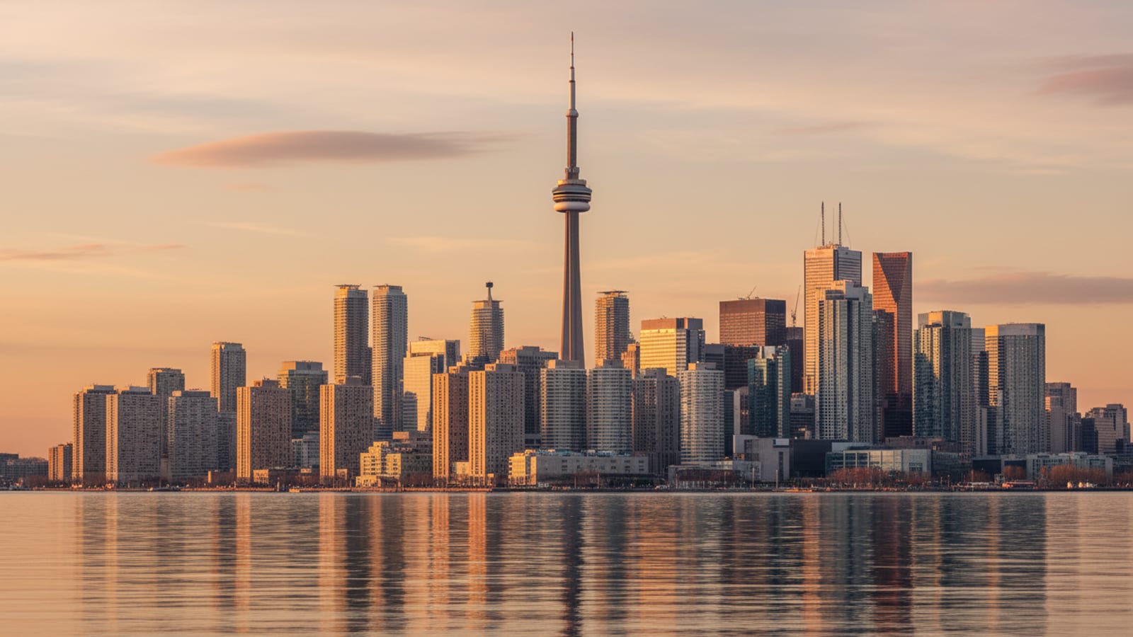 The Toronto downtown skyline and CN Tower at golden hour, with Lake Ontario calm in the foreground